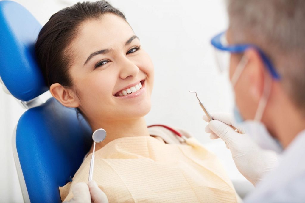 A woman in a dentists chair smiling.