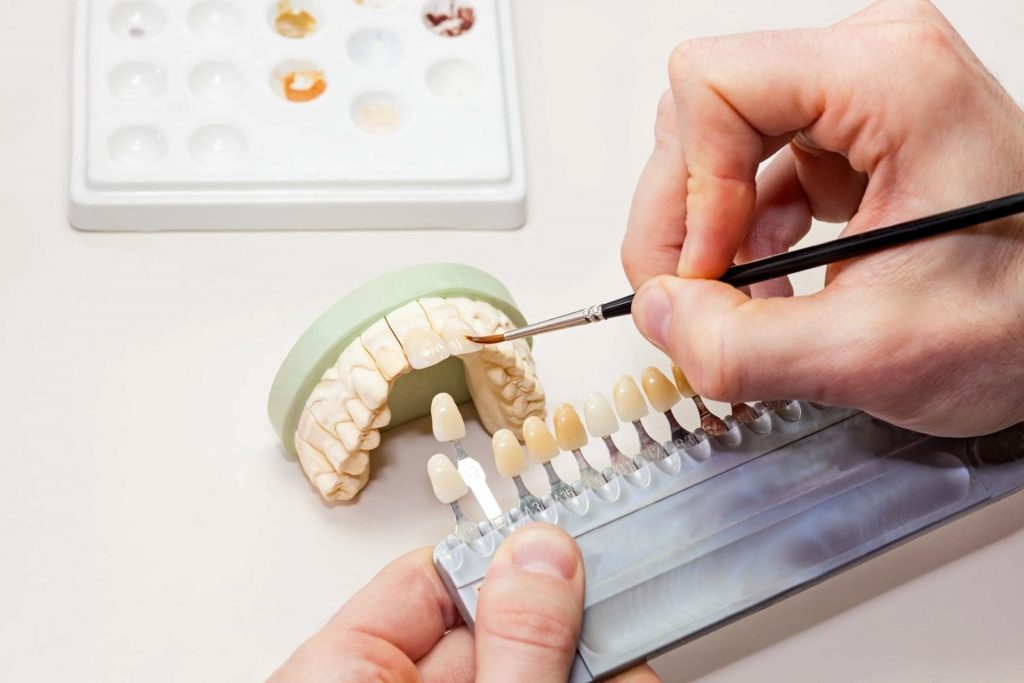 A dentist using a small paintbrush on a set of dentures.