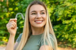 Woman holding a clear orthodontic aligner against green foliage background
